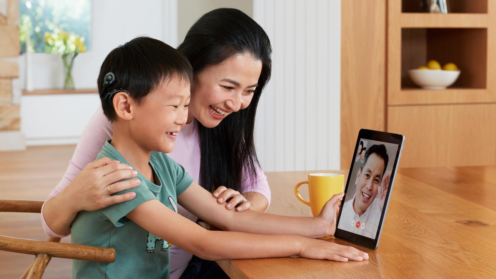 Băiat asiatic cu procesor de sunet Nucleus vorbind cu tatăl său prin Facetime