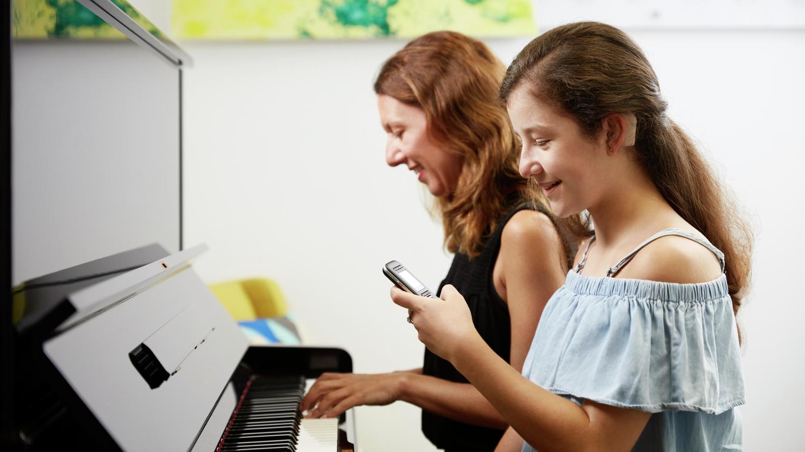 Teini-ikäinen tyttö käyttää mikrofonia samalla, kun hänen äitinsä soittaa pianoa