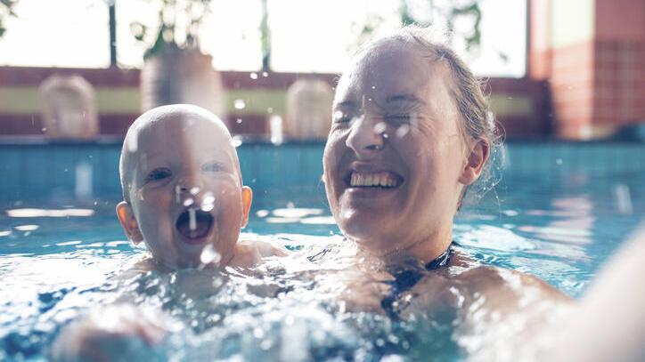 A woman and a baby splash water in a swimming pool
